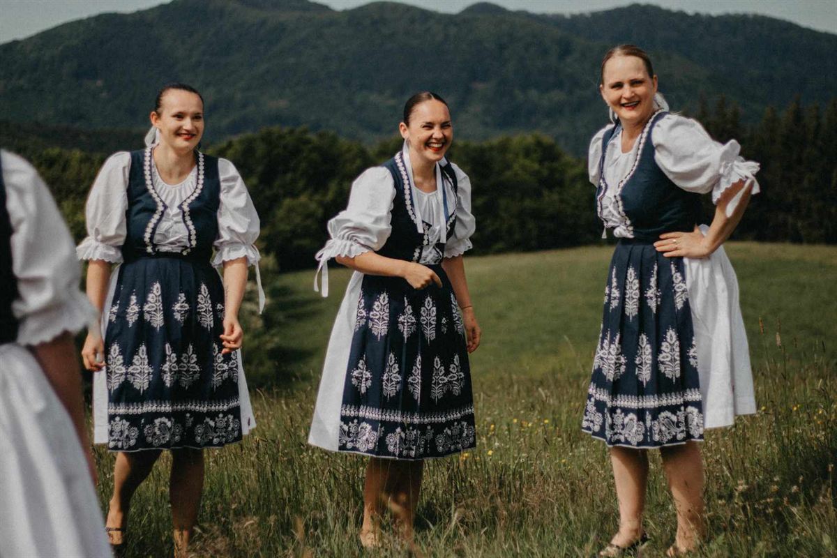 Tri členky súboru v modrotlačových krojoch na lúke pod horami